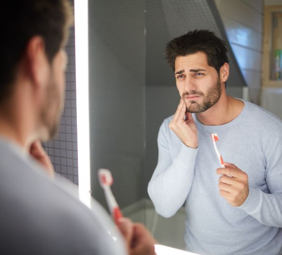 Man holding toothbrush rubbing jaw in pain