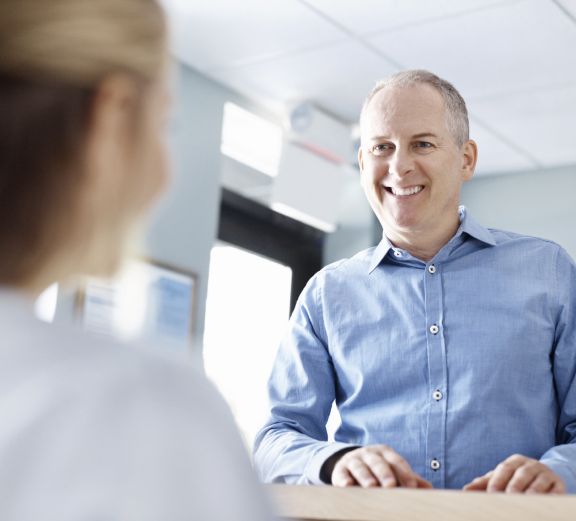 Smiling man talking to dental team member at front desk